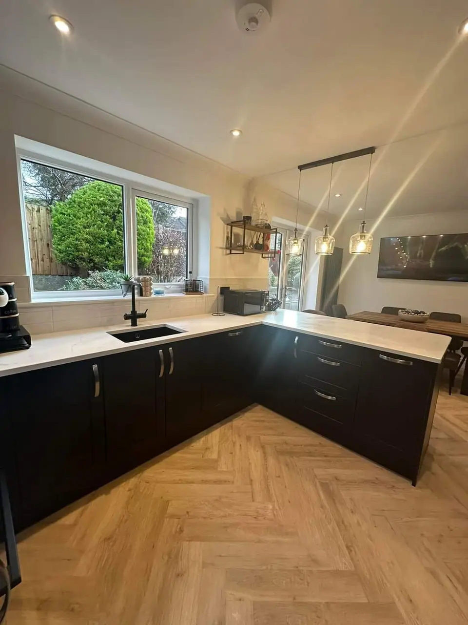A finished kitchen with dark units, a white worktop, pendant lights and a herringbone floor