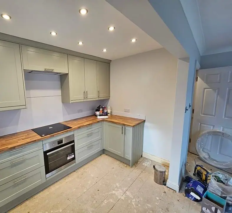 Sage-green kitchen units with an oak worktop and oven installed, with the floor not yet finished