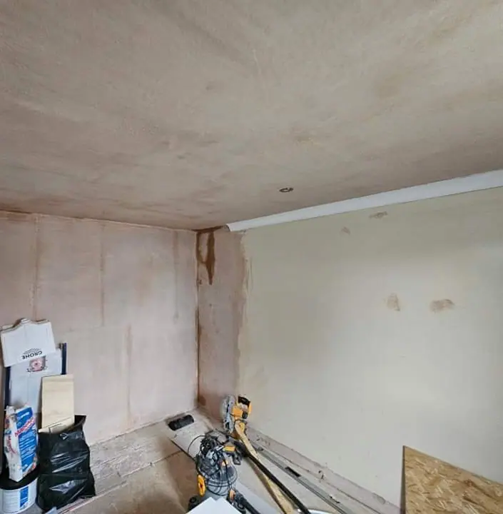 A room mid-refurbishment with freshly plastered ceiling and walls, tools and materials on the floor
