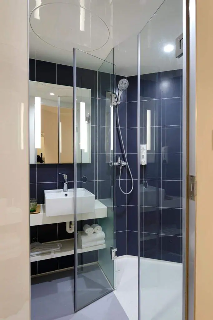 A finished shower room with blue tiled walls, a glass shower enclosure, a basin and an illuminated mirror