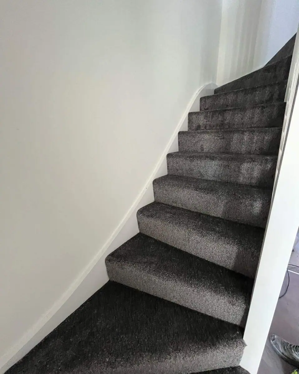 A staircase with grey carpet, white painted walls and skirting