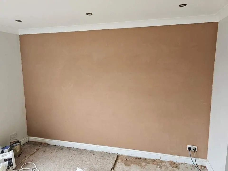 A wall with a fresh brown plaster base coat beneath coving and ceiling downlights, with the carpet lifted